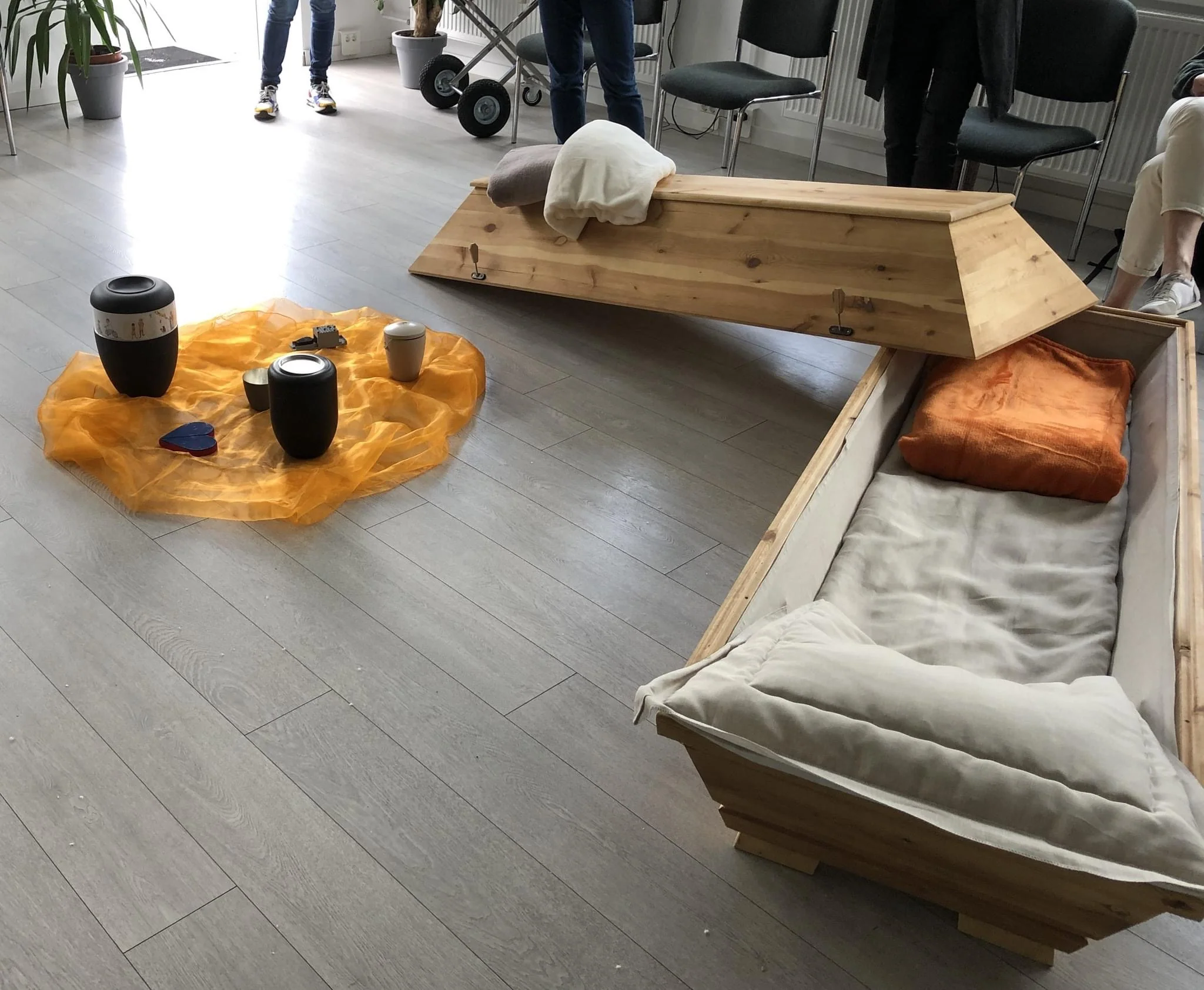 Ein offener Holzsarg mit Decke und Kissen steht bei einer Fortbildungsveranstaltung in einem Raum.