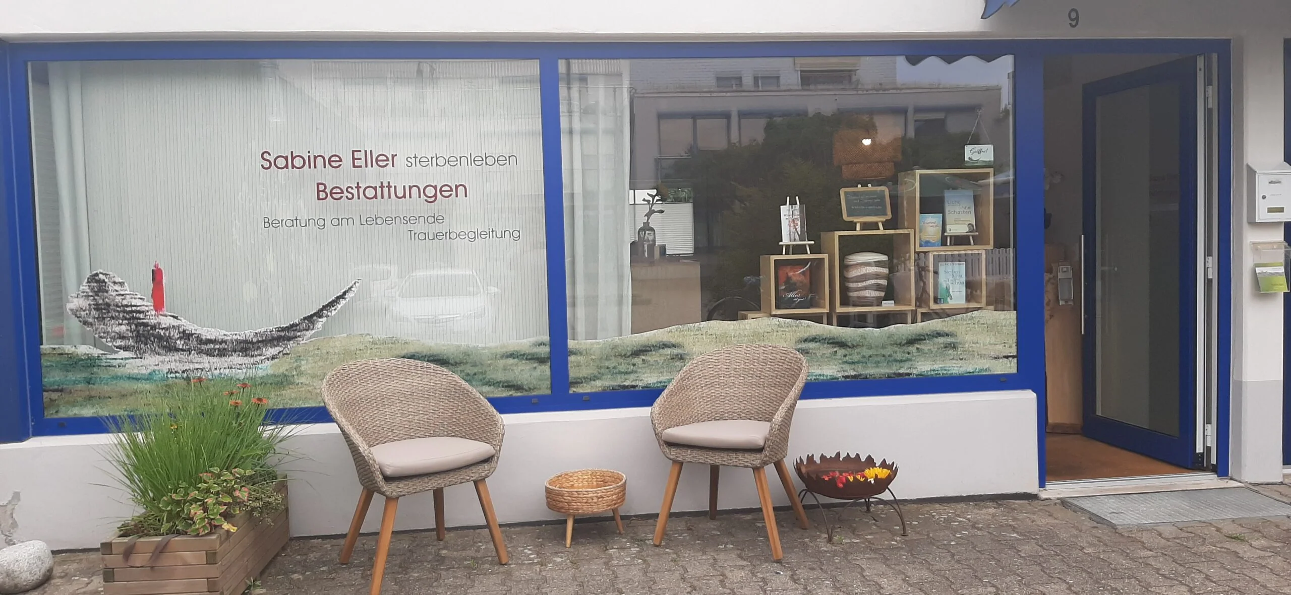 Schaufenster von sterbenleben mit zwei Stühlen und Pflanzen vor dem Eingang.